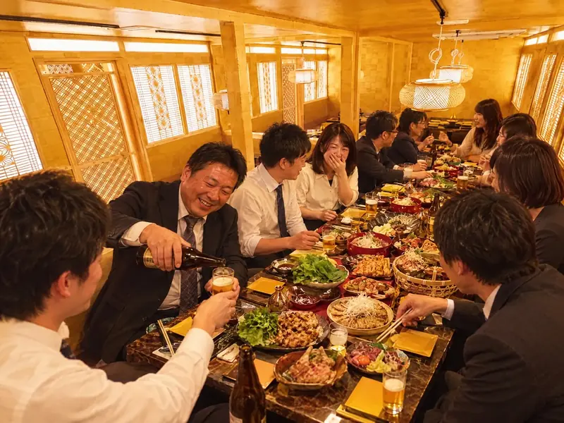 大皿料理を囲む会社の宴会（イメージ）